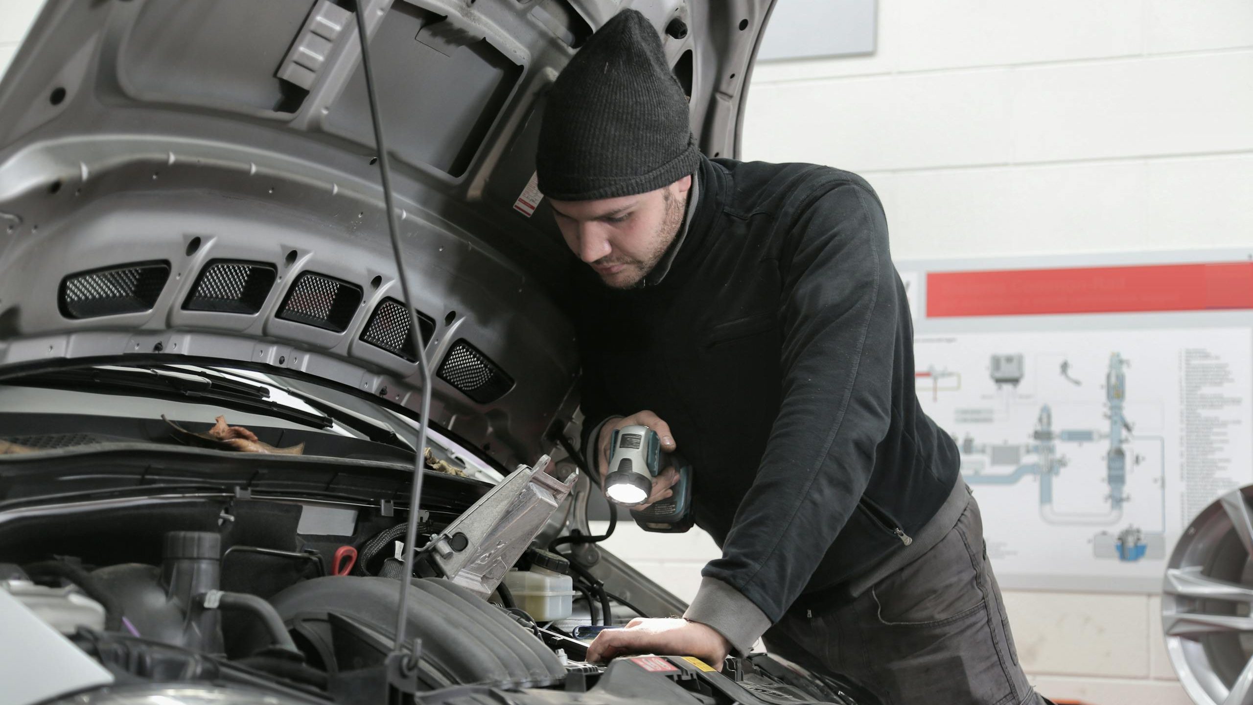 A mechanic closely inspects a car engine in a garage using a flashlight, ensuring proper maintenance.