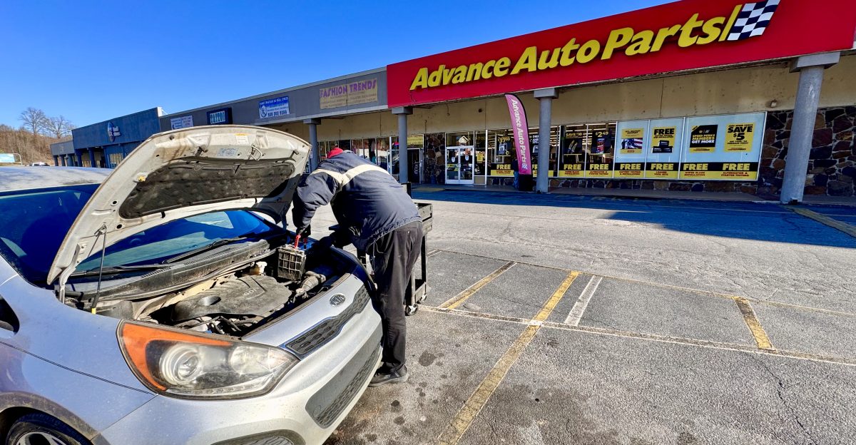 An Advance Auto Parts store employee changes a car battery in a parking lot in front of the shop