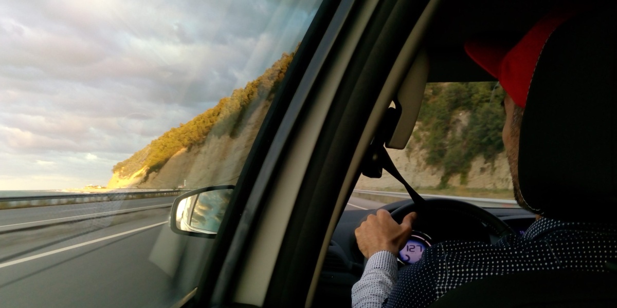 a shot from the backseat of a man in a red hat driving a car on the road