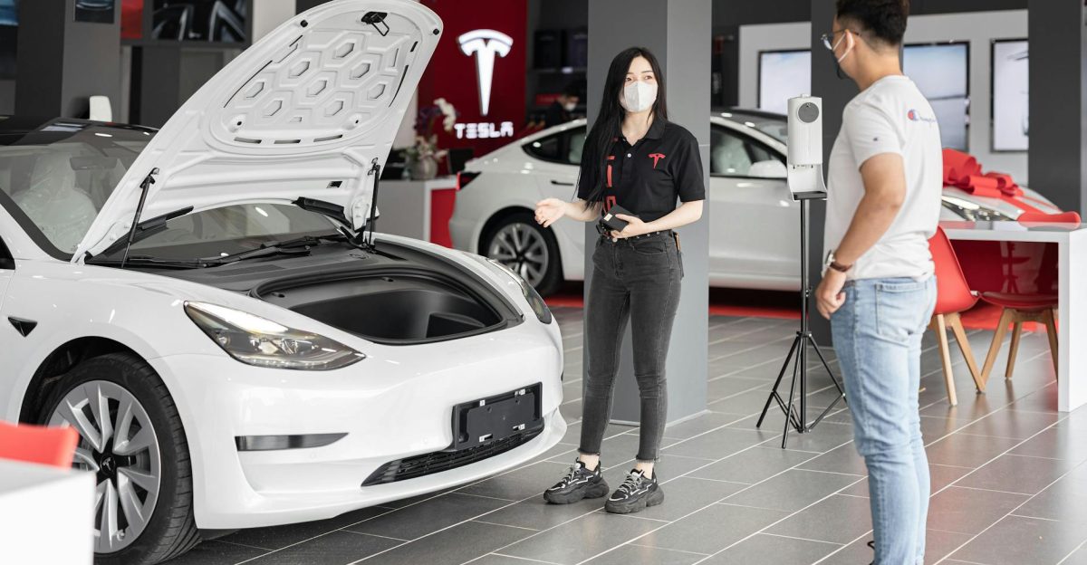 A customer talks with a sales representative about a Tesla Model 3 in a car dealership showcasing the electric car s features