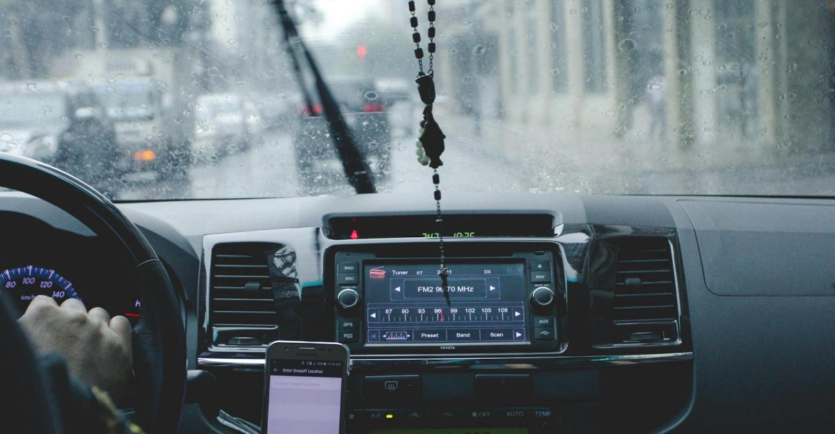 Car interior with driver navigating rainy cityscape using phone and dashboard