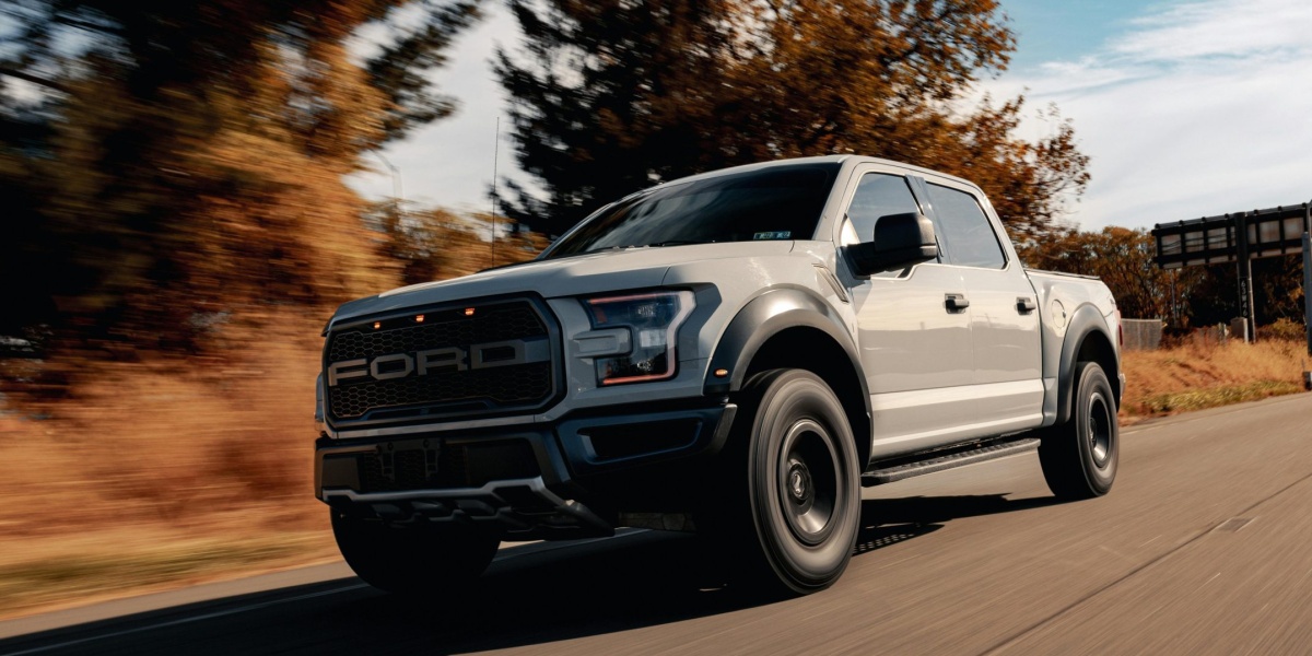 A Ford F-150 driving on a scenic highway surrounded by trees and blue skies.