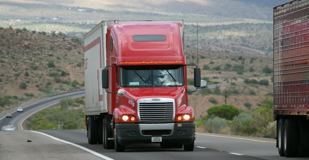 Red semi-truck driving through scenic highway in a mountainous landscape