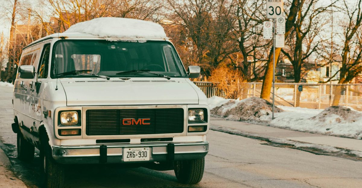 Vintage GMC van covered with snow parked on a snowy street intersection with winter trees around