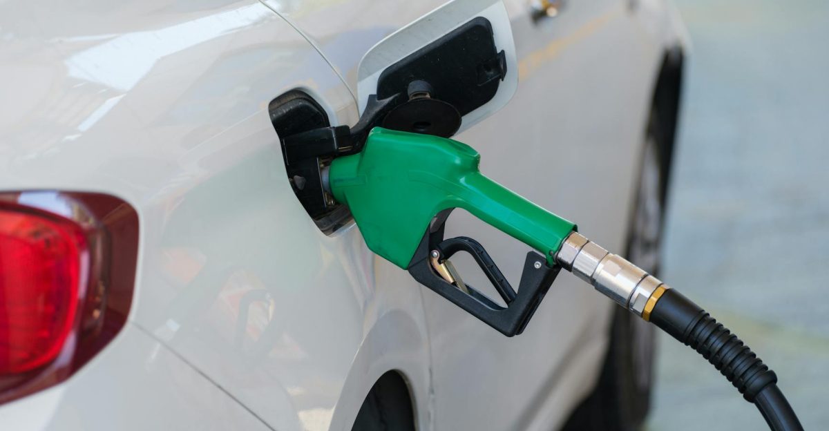 Close-up of a green nozzle refueling a white car at a gas station