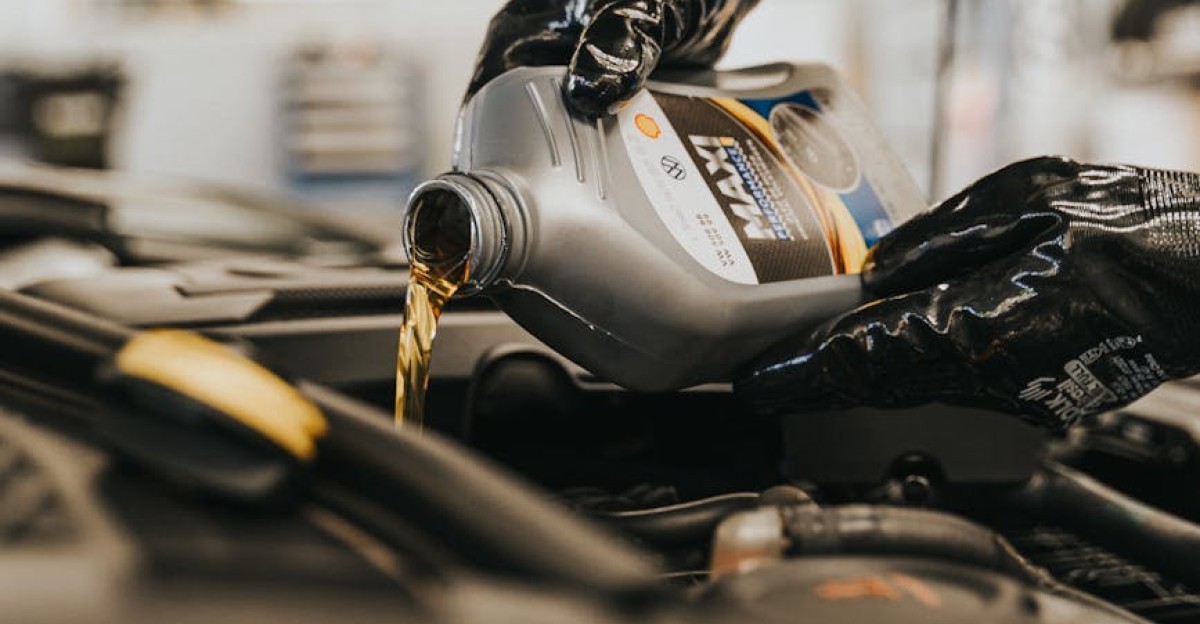 Close-up of a mechanic pouring engine oil into a car engine with gloved hands indoors