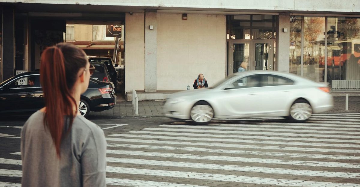 A woman stands at a city pedestrian crossing as cars pass by