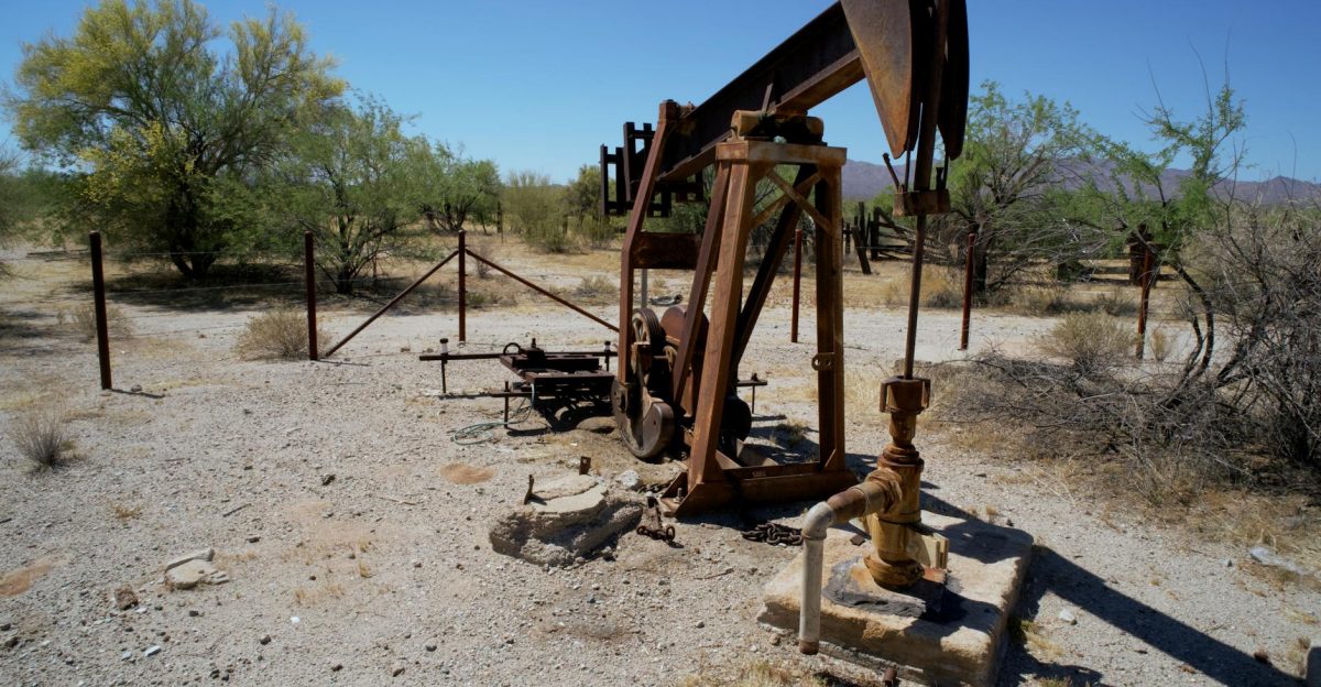 Rusted pumpjack in arid desert setting with sparse vegetation and clear sky