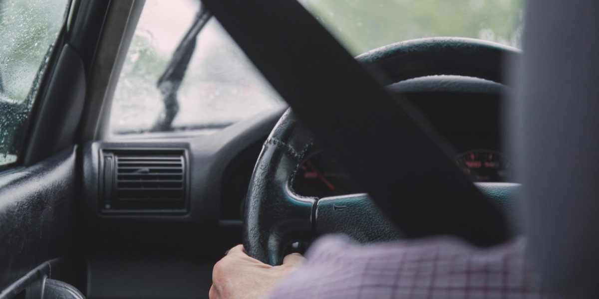 Interior view of a car during rainy weather, emphasizing safety with visible seat belt and driver focused on road.