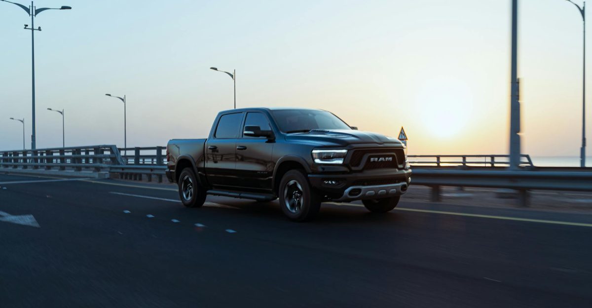 A sleek black Ram pickup truck speeds down an empty highway at sunrise showcasing modern design and power