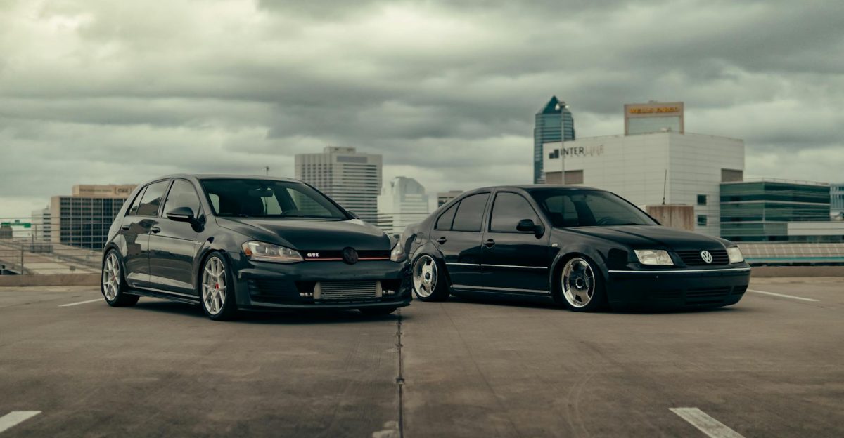 Two Volkswagen cars parked in an urban rooftop parking lot with a city skyline in the background