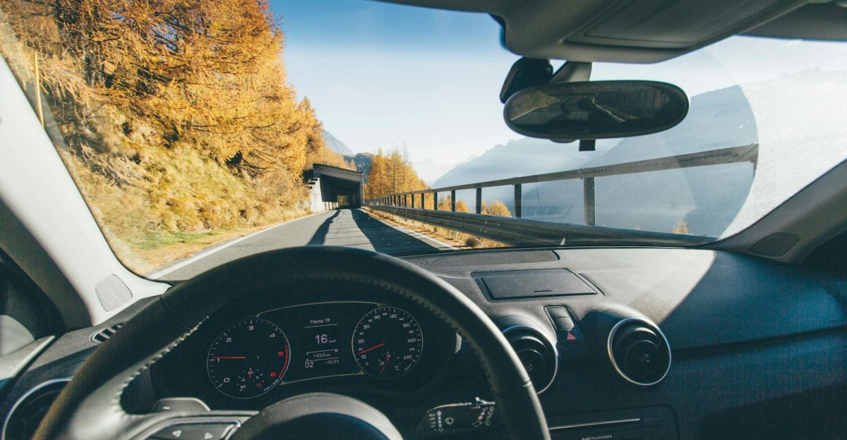 View from car interior driving through a scenic mountain road with autumn foliage and clear skies