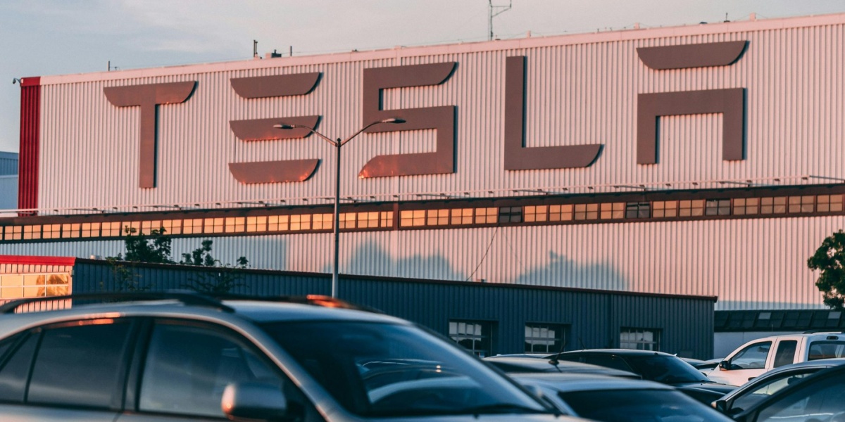 Tesla factory with parked cars during sunset, showcasing modern automotive industry vibes.