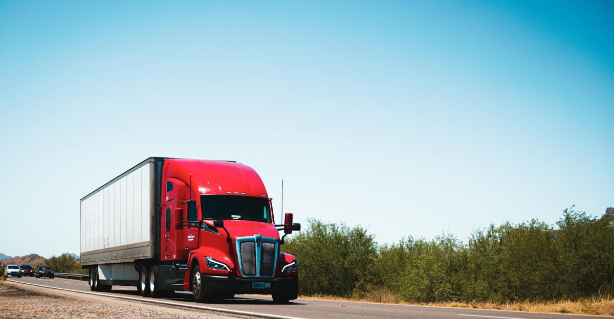 Vibrant red semi-trailer truck driving on an open highway under a clear blue sky