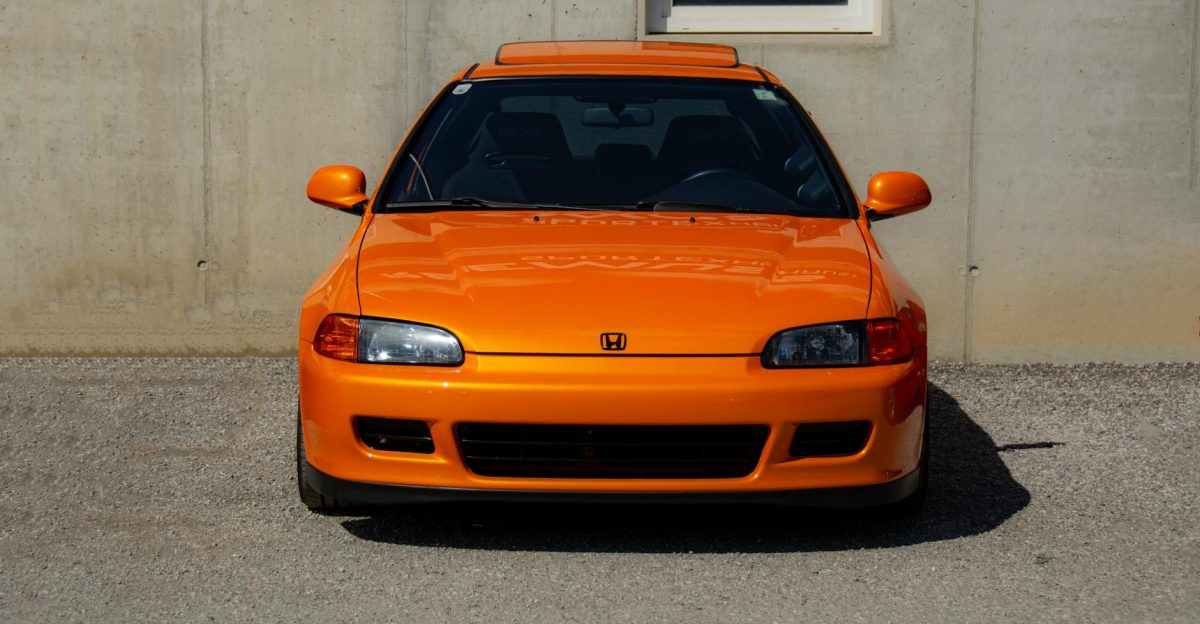 A vibrant orange Honda Civic parked outdoors at a car meet in Austria