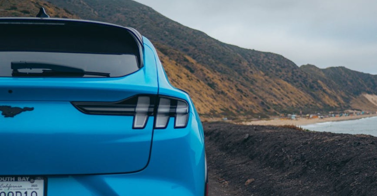 A blue electric SUV parked on a rugged coastal highway capturing scenic ocean views