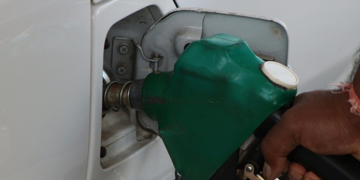 Close-up of a hand refilling a car's gas tank at a station with a green fuel nozzle.
