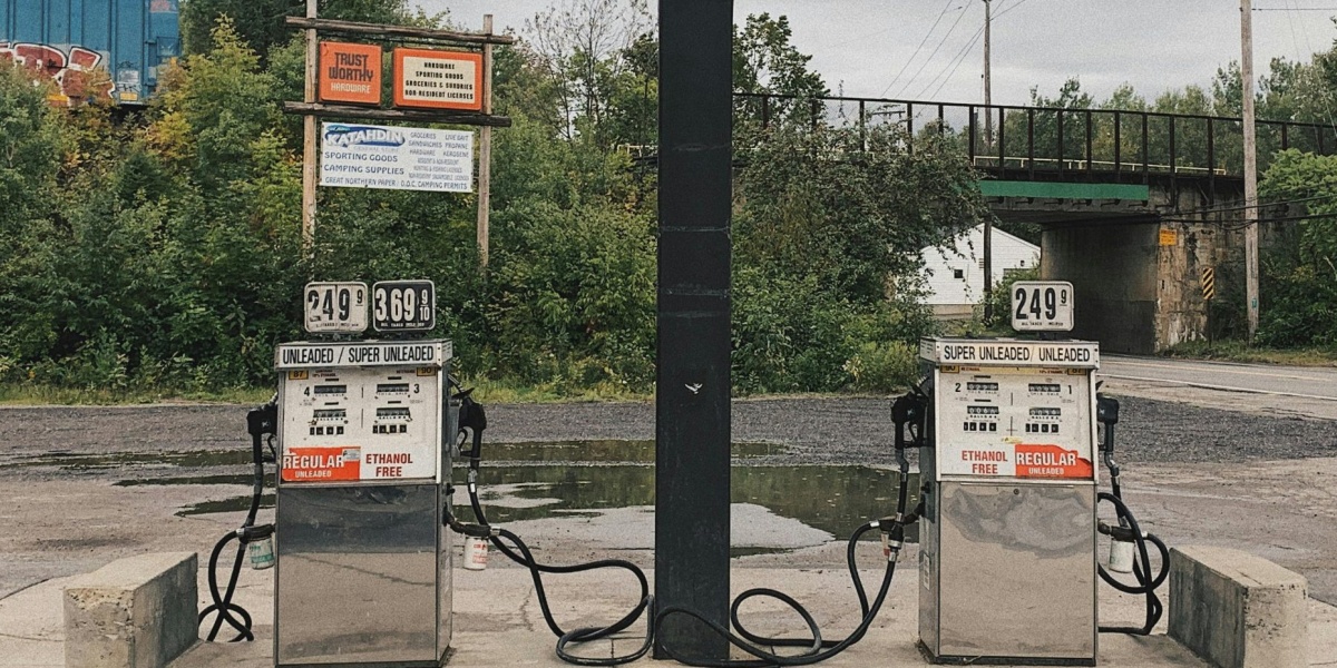 An outdoor scene of an abandoned gas station with dual pumps and vivid greenery in the background.