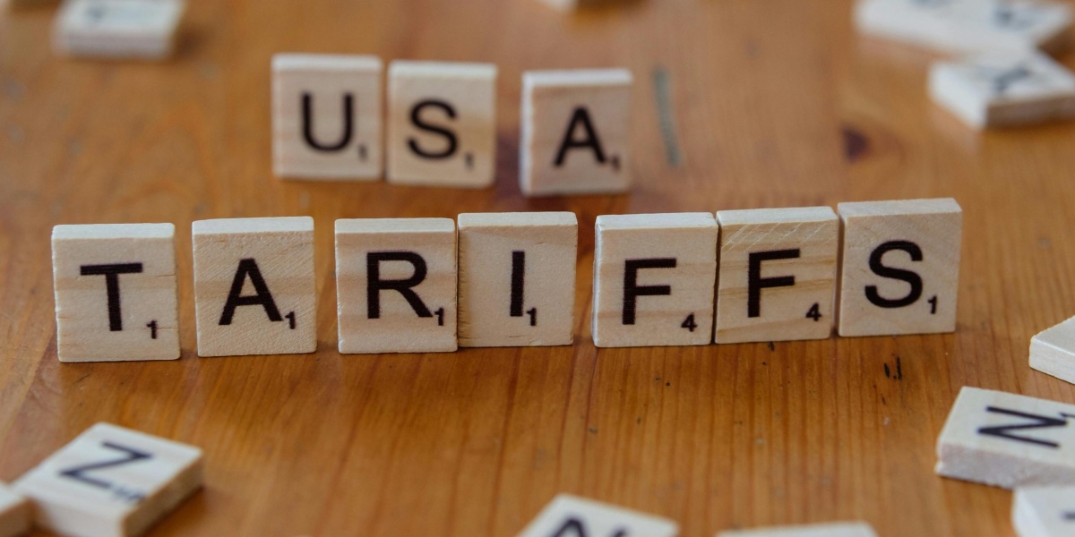 Wooden tiles spelling 'USA' and 'TARIFFS' on a wooden surface symbolizing trade issues.