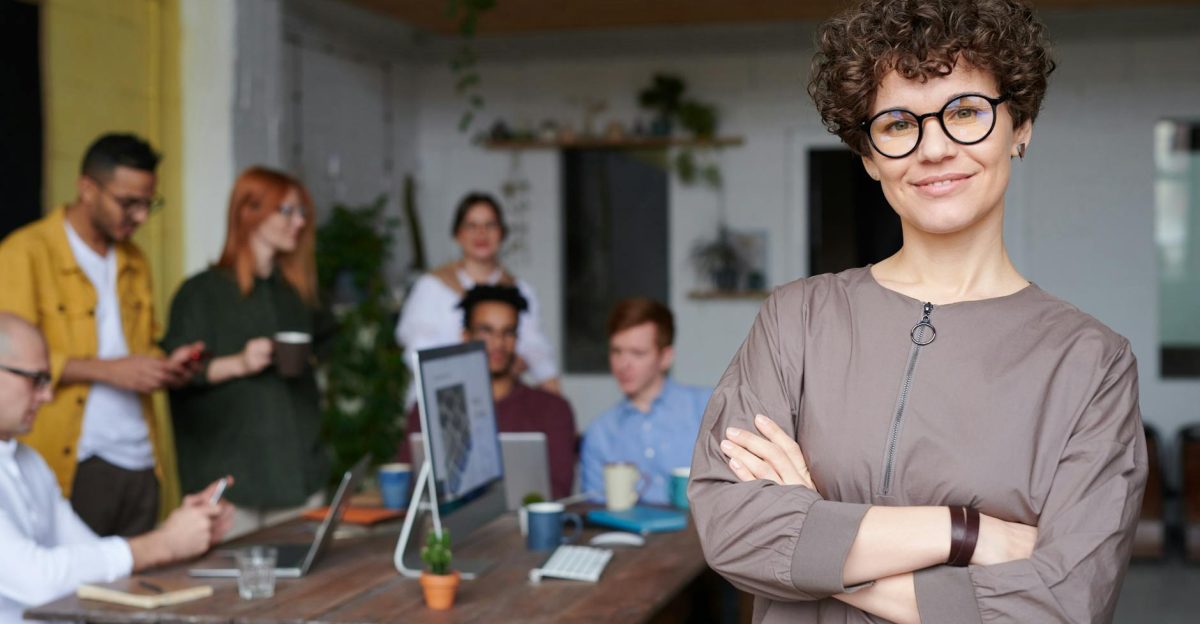 Smiling businesswoman with curly hair stands confidently in a modern office space with colleagues