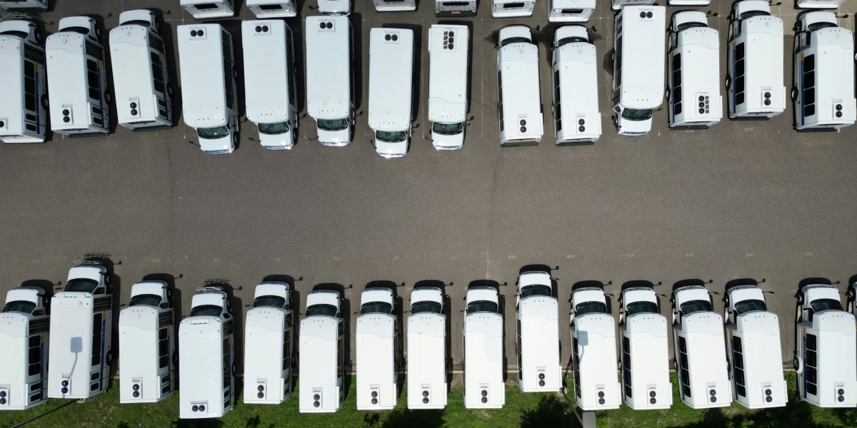 Aerial view of a large parking lot filled with white vans on a sunny day.