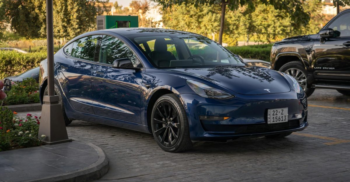 Electric blue Tesla Model 3 parked in sunlit commercial parking area