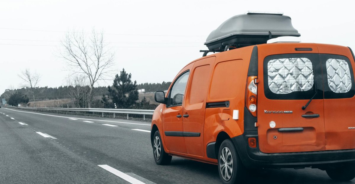 Bright orange van traveling on an empty highway with a roof box on a cloudy day