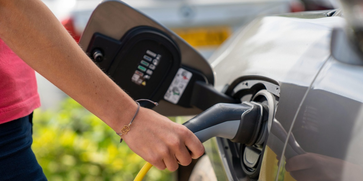 Close-up of a person plugging in an electric car at a charging station outdoors.