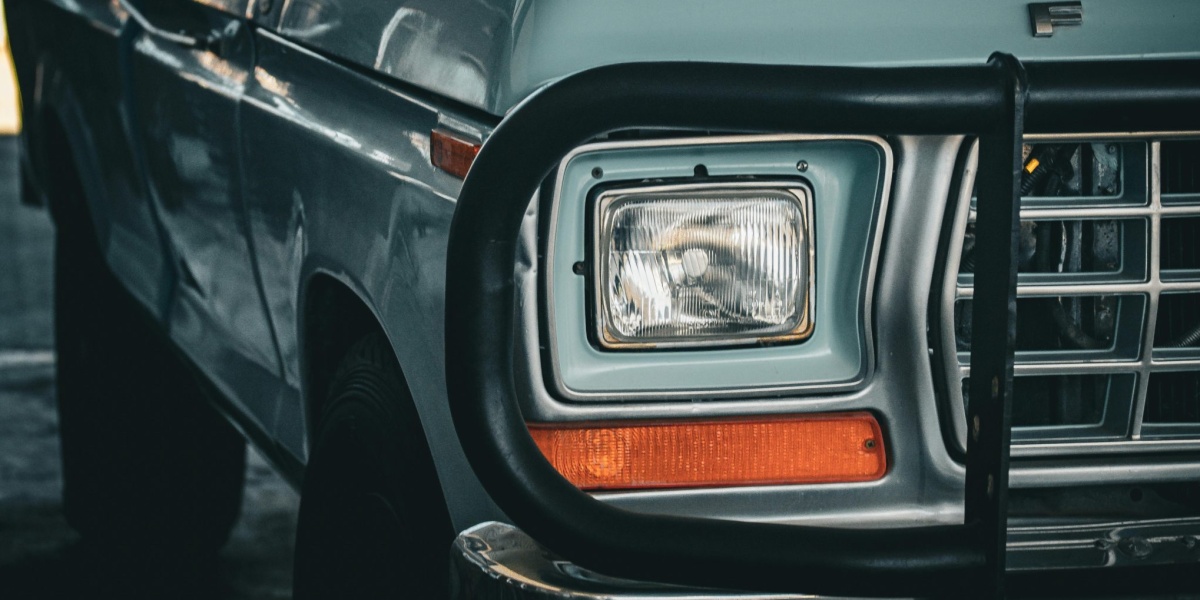 Close-up of a vintage Ford truck showcasing the front grille and headlight in a shadowy environment.