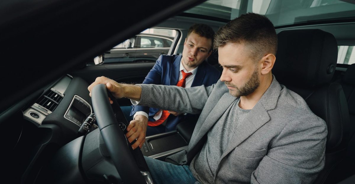 Salesman demonstrating car features to potential buyer inside vehicle showroom