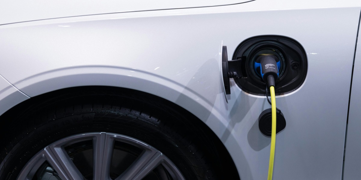 A white electric car is plugged in for charging, close-up view of the charging port.