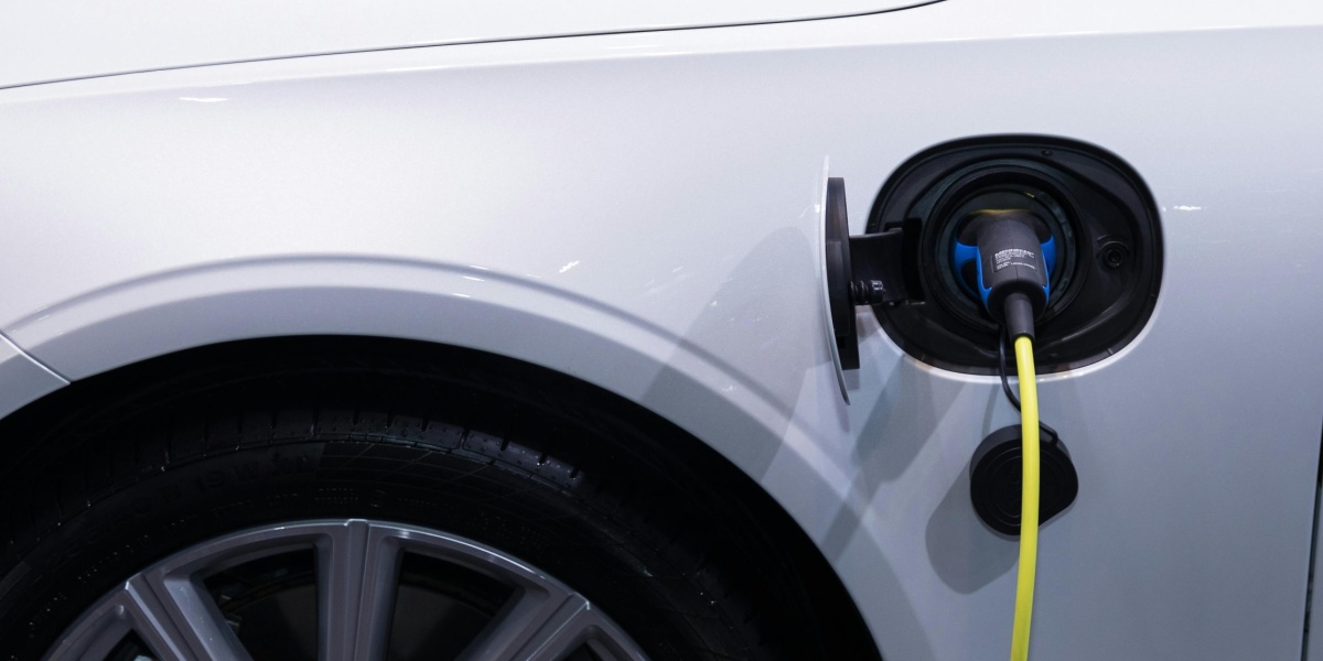 A white electric car is plugged in for charging, close-up view of the charging port.