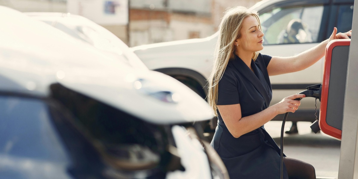 A woman charges her electric car at a city station, embracing eco-friendly travel.