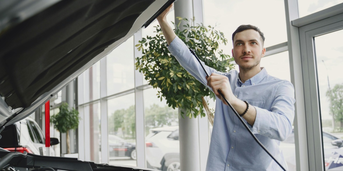 A man carefully checking a car engine in a bright, modern car showroom.