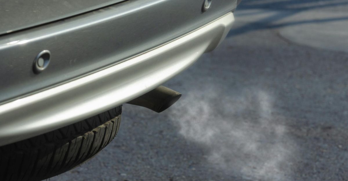 Close-up of a silver car exhaust pipe emitting smoke on asphalt road