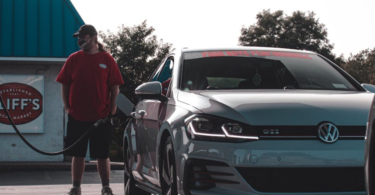 A man in red shirt refuels a Volkswagen GTI at an outdoor gas station during the day