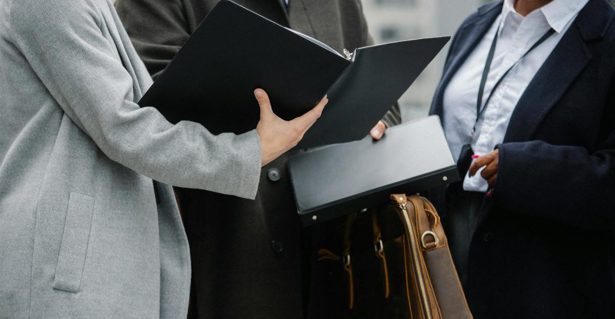 Crop diverse coworkers wearing formal outfits reading documents together and discussing project on street