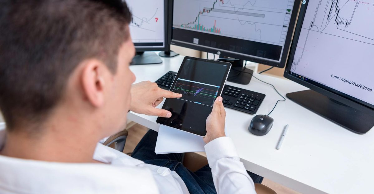 A stock trader analyzing cryptocurrency charts on multiple monitors and a tablet