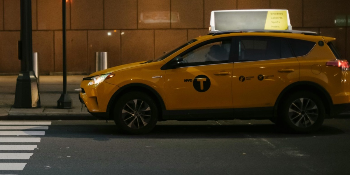 Modern shiny yellow SUV taxi car stopped near traffic light at zebra crossing in evening