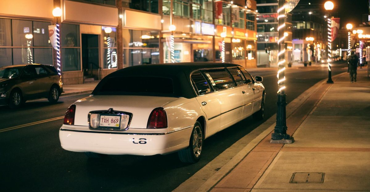 White limo with tinted glasses and license plate on roadway against buildings illuminated by street lights in evening city