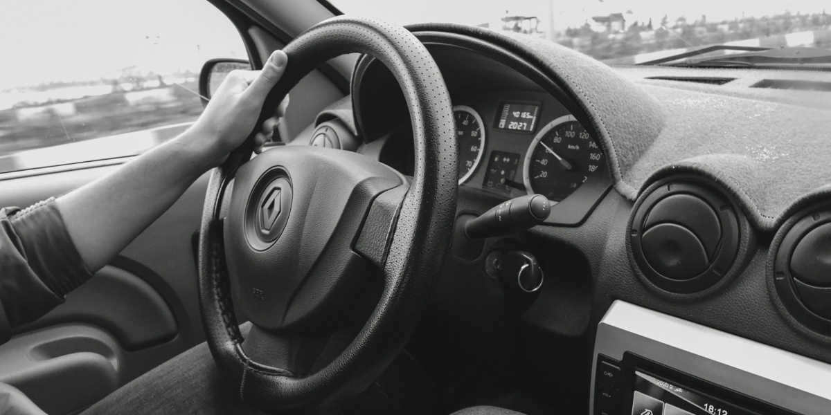 Monochrome view of a person driving a car, focusing on steering and dashboard details.