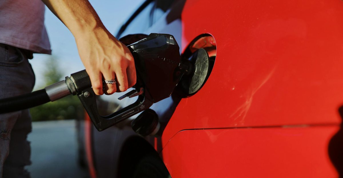 Close-up of a person refueling a red car at an outdoor gas station during the day