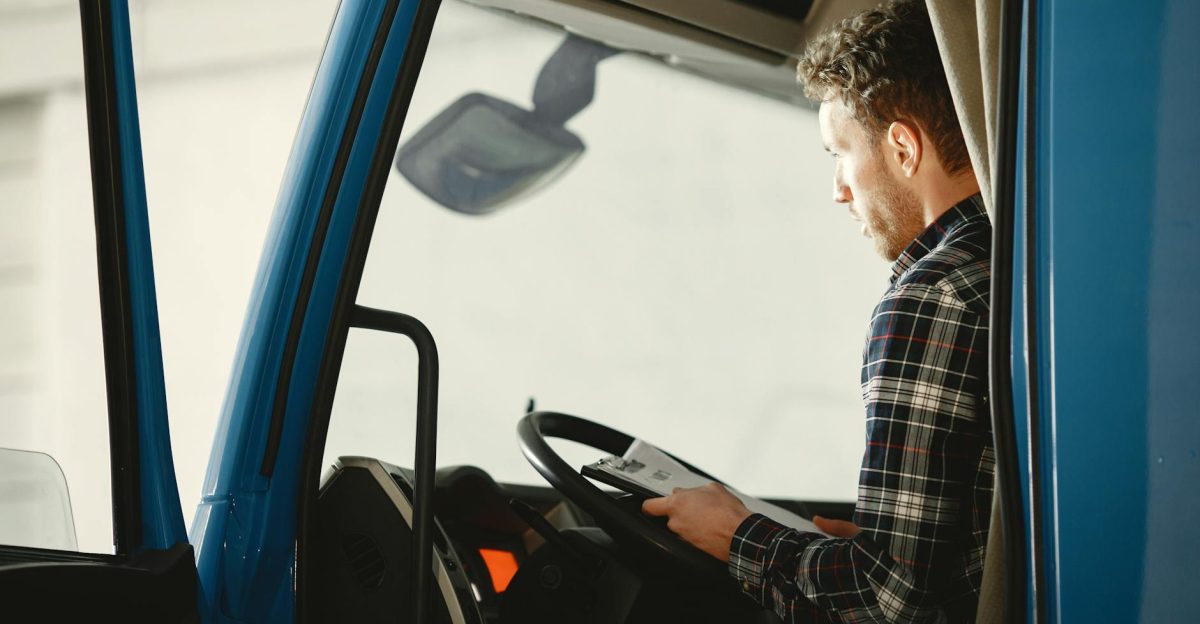 A man sitting in a truck cabin reading a document inside a blue truck showcasing focused driving preparation