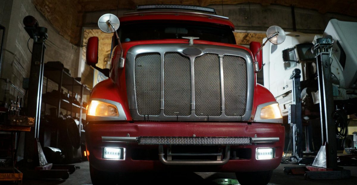 Front view of a red truck in a dimly lit automotive repair shop with a focus on the grill and headlights