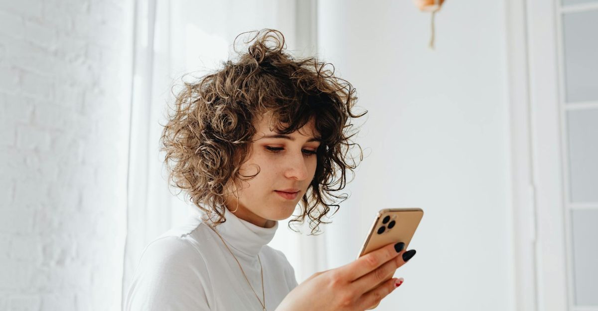 A young woman with curly hair using a smartphone indoors Natural light and modern decor