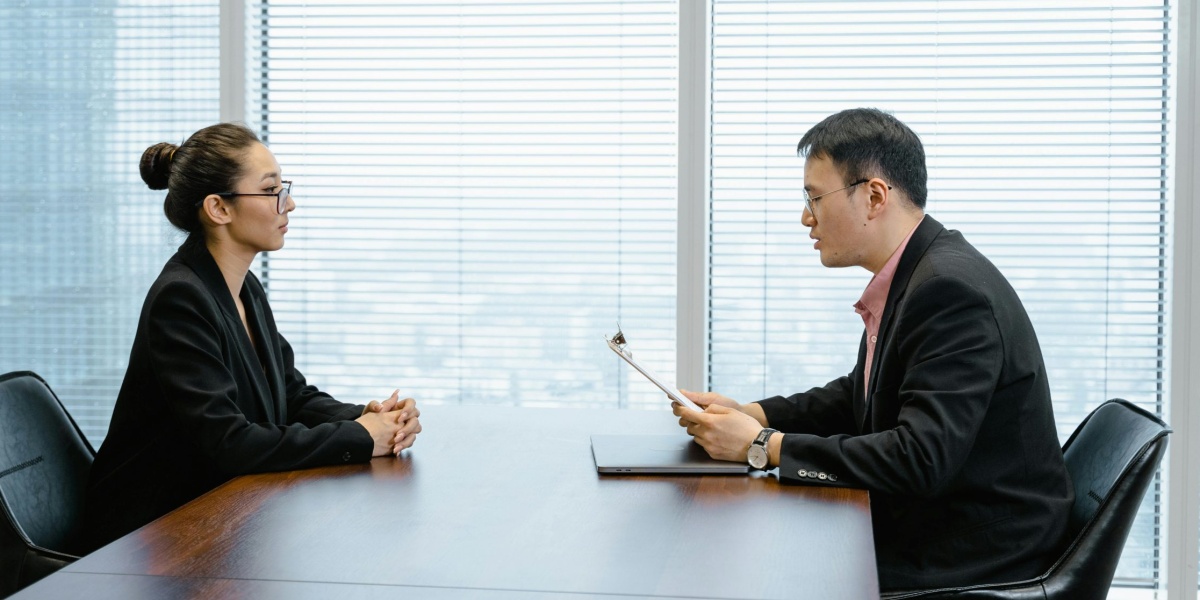 Two professionals in a business meeting in a modern office, facing each other across a table.