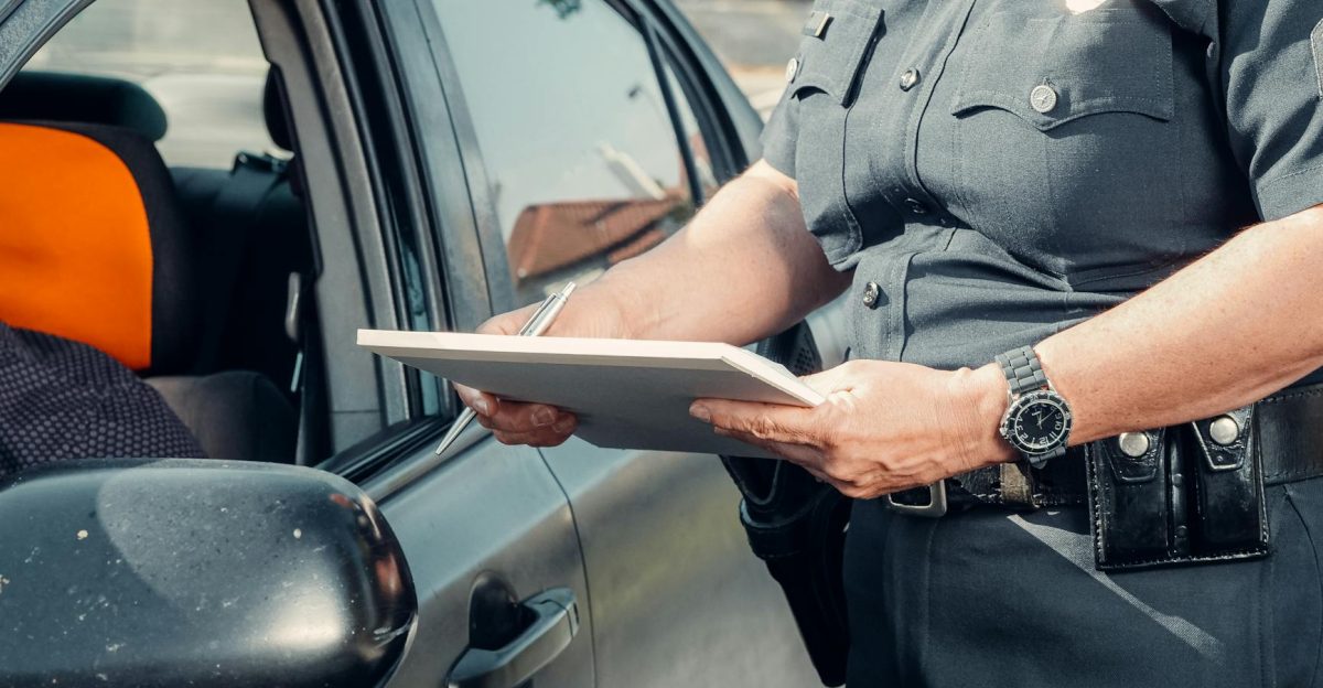 A police officer in uniform writes a ticket to a driver through the car window on a sunny day