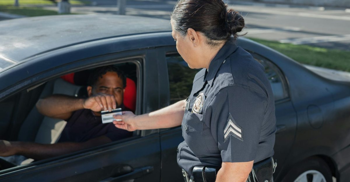 A police officer hands a ticket to a driver in a car on a sunny day street