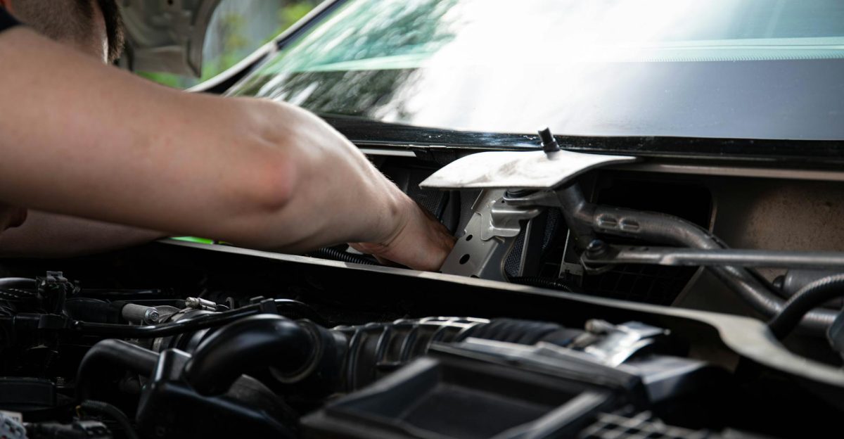 Mechanic performing engine maintenance on a car outdoors focusing on repair work