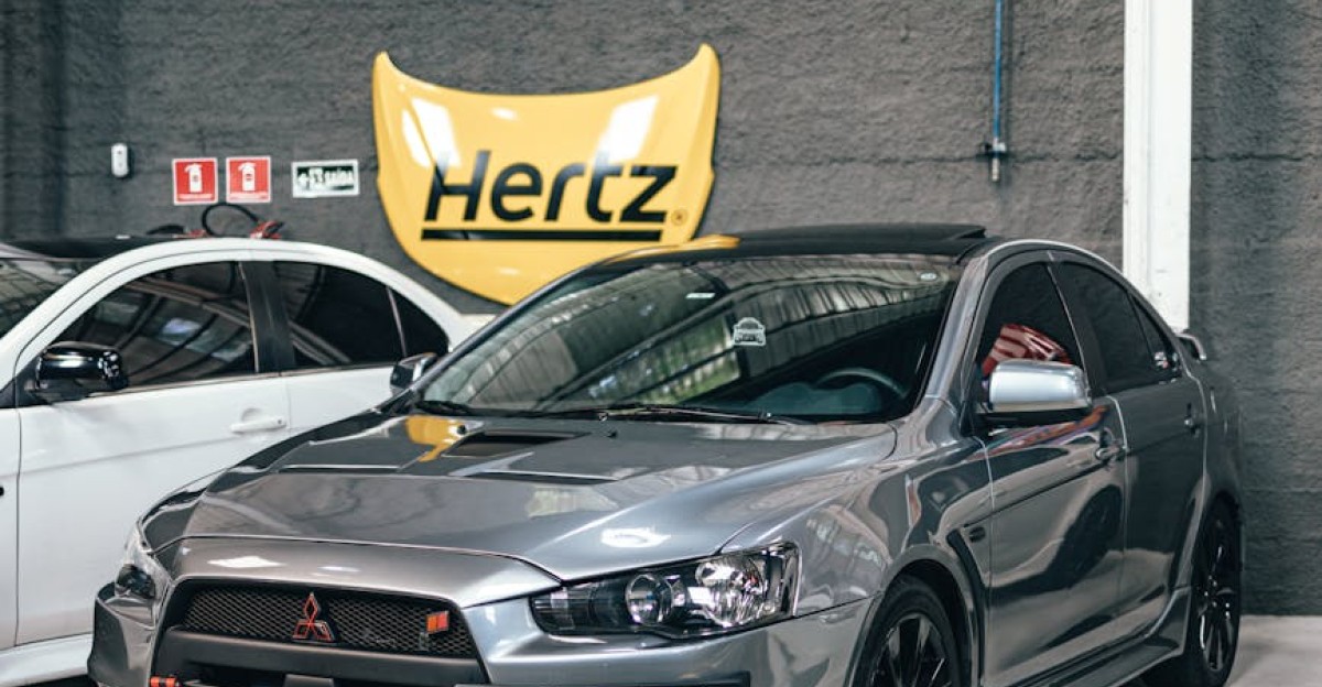 Gray Mitsubishi Evo parked in a well-lit indoor garage with Hertz signage in the background